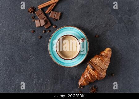 Tazza di caffè con cannella e spezie all'anice, pezzi di cioccolato e croissant su sfondo nero vista dall'alto. Orientamento orizzontale. Foto Stock
