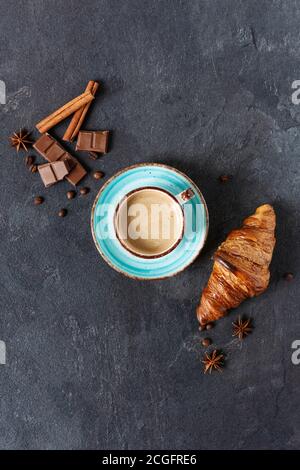 Tazza di caffè con cannella e spezie all'anice, pezzi di cioccolato e croissant su sfondo nero vista dall'alto. Orientamento verticale. Foto Stock