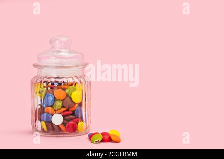 Caramelle di cioccolato a guscio duro in un vaso di cristallo e sopra uno sfondo rosa con spazio per la copia Foto Stock