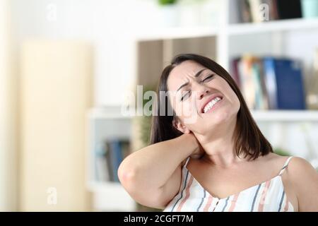 Donna stressata che soffre di dolore al collo nel soggiorno a. casa Foto Stock