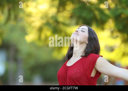 Donna rilassata in rosso che respira aria profondamente fresca in piedi dentro un parco Foto Stock