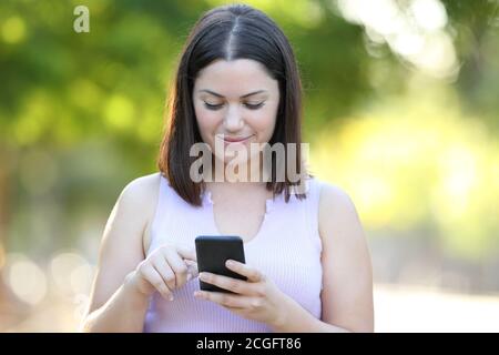 Vista frontale ritratto di una donna seria che utilizza uno smartphone passeggiate in un parco Foto Stock