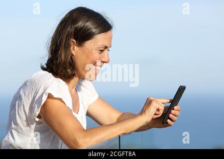 Donna adulta felice usa lo smartphone su un balcone su la spiaggia Foto Stock