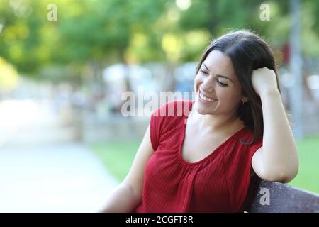 Donna felice rilassante contemplando seduta su una panchina in un parcheggio Foto Stock