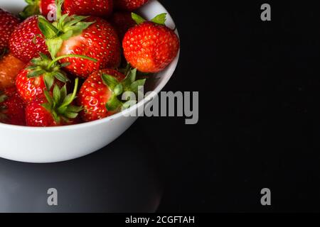 Alcune fragole mature giacciono su un piatto bianco profondo Su vetro nero.posizionare per una copia dello spazio Foto Stock