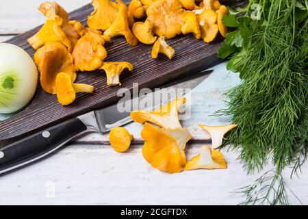 I funghi chanterelle giacciono su una tavola di legno scuro, una testa di cipolle e grappoli di aneto e prezzemolo giacciono sul tavolo. L'autunno sta arrivando Foto Stock