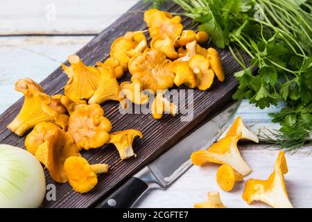 I funghi chanterelle giacciono su una tavola di legno scuro, una testa di cipolle e grappoli di aneto e prezzemolo giacciono sul tavolo. L'autunno sta arrivando Foto Stock