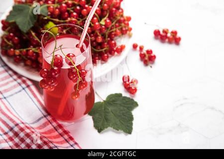 Ciuffi di bacche di ribes rosso giacciono in un piatto bianco su un tovagliolo a scacchi rosso e bianco, una Morse bacche si trova in un vetro su uno sfondo chiaro. S Foto Stock