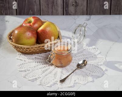 Un vasetto di mele e applique in un piatto di vimini su uno sfondo chiaro su un tovagliolo di pizzo. Orientamento orizzontale Foto Stock