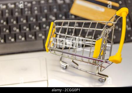 computer portatile con un piccolo carrello giallo e una carta di credito primo piano. Il concetto di shopping online Foto Stock