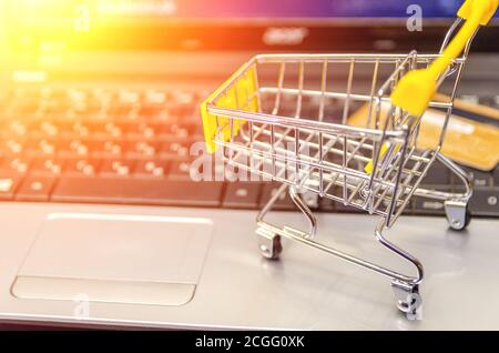computer portatile con un piccolo carrello giallo e una carta di credito primo piano. Il concetto di shopping online Foto Stock