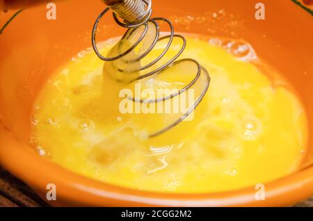 Montare i tuorli in una terrina di argilla con una frusta primo piano Foto Stock