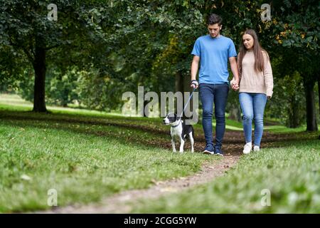 Giovane coppia che cammina il loro cane animale domestico lungo il percorso nel parcheggio Foto Stock