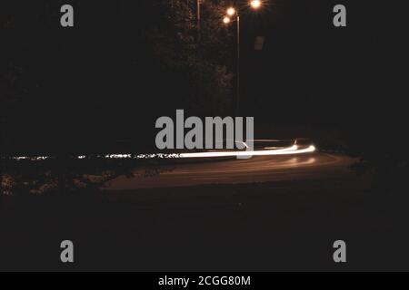 Luci notturne dei fari mistici dell'auto sulla banda autostradale su lunga esposizione. Luce a movimento rapido che illumina la città buia Foto Stock