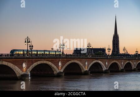 Luci di strada illuminate al tramonto, tram che attraversa il ponte Pont de Pierre sullo sfondo, Bordeaux, Francia. Foto Stock