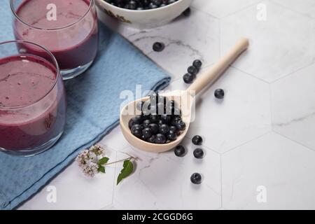 Su uno sfondo chiaro è un cucchiaio di legno con mirtilli, due bicchieri con una dieta frullato di mirtillo sono su un tovagliolo blu . Spazio per la copia Foto Stock