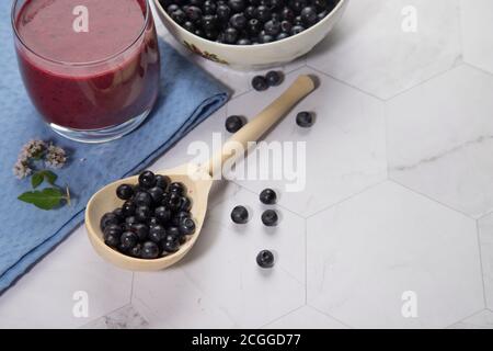 Su uno sfondo chiaro è un cucchiaio di legno con mirtilli, due bicchieri con una dieta frullato di mirtillo sono su un tovagliolo blu . Spazio per la copia Foto Stock