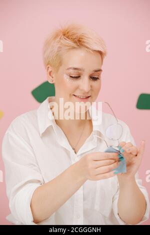 Giovane donna sorridente con capelli biondi corti tinti occhio stelle bicchieri per la pulizia del trucco Foto Stock