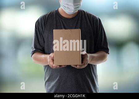Addetto alla consegna che tiene scatole di cartone e accetta l'addetto alla consegna maschera protettiva Foto Stock