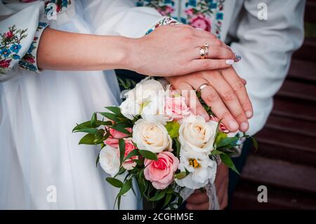 mani di sposi novelli con anelli di nozze su un bouquet di nozze con rose bianche e rosa Foto Stock