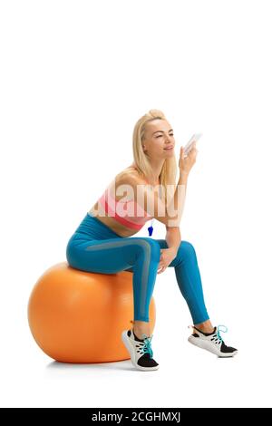 Registrazione della voce su FIT Ball. Bella allenatore di fitness femminile che pratica isolato su sfondo bianco studio. Modello biondo caucasico in outfit sportivo. Occupazione professionale, stile di vita attivo e sano. Foto Stock