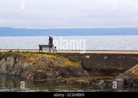 17 giugno 2020 UN uomo anziano solista cammina lungo il Muro di cemento che fa parte dell'antico Long Hole Porto nella contea di Bangor, in fondo all'Irlanda del Nord Foto Stock