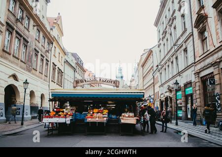 Praga, Czechia - Vista frontale del Havelské tržiště, il mercato più antico della capitale, con chioschi che vendono frutta e cereali con alcuni clienti Foto Stock