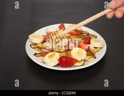 Cibo alla moda - cereali pancake. Un mucchio di mini frittelle di cereali su un piatto bianco, spazio di copia. Fragole, banane e miele. Una bella e sana Bre Foto Stock