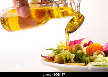 Versare l'olio d'oliva dal distributore dell'olio sull'insalata preparata piastra bianca e sfondo isolato Foto Stock