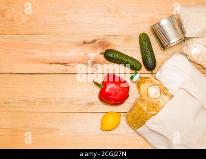 Il concetto di evitare sacchetti di plastica, consumo consapevole. Cibo in una borsa di stoffa su sfondo di legno, vista dall'alto, spazio libero per il testo. Foto Stock