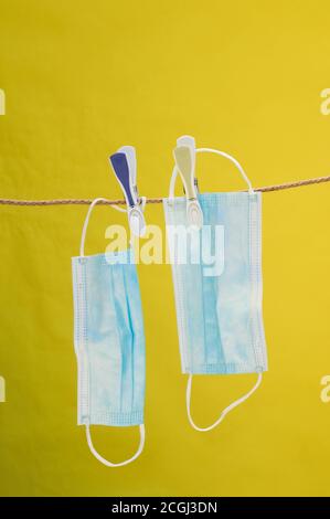 foto verticale dell'asciugatura di due maschere blu monouso una corda fissata con i clothespins sopra lo sfondo giallo Foto Stock