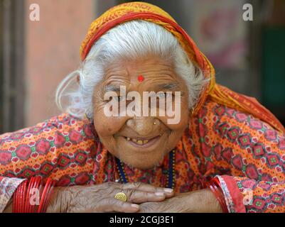 La vecchia donna nepalese Chhetri si pone per la fotocamera con entrambe le braccia ripiegate sul tavolo. Foto Stock