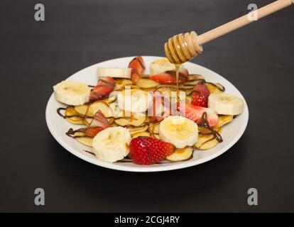 Cibo alla moda - cereali pancake. Un mucchio di mini frittelle di cereali su un piatto bianco, spazio di copia. Fragole, banane e miele. Una bella e sana Bre Foto Stock