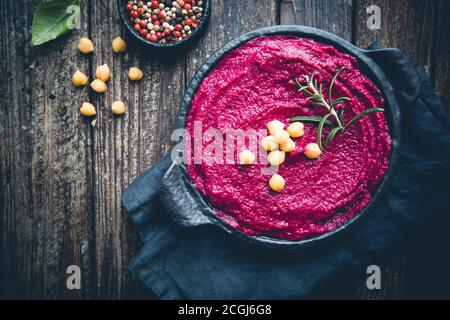 Rosso di barbabietola hummus, cremoso e delizioso in un vaso nero più scuro dello sfondo in legno, vista dall'alto Foto Stock