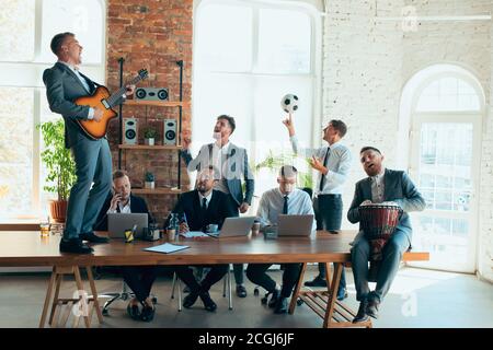 Cantare, dare concerti di musica, ballare. I colleghi sono felici e spensierati e si divertono in ufficio mentre i colleghi lavorano sodo e altamente concentrati. Concetto di divertimento, riposo, occupazione professionale. Foto Stock