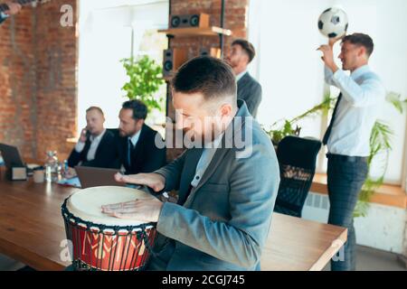 Cantare, dare concerti di musica, ballare. I colleghi sono felici e spensierati e si divertono in ufficio mentre i colleghi lavorano sodo e altamente concentrati. Concetto di divertimento, riposo, occupazione professionale. Foto Stock