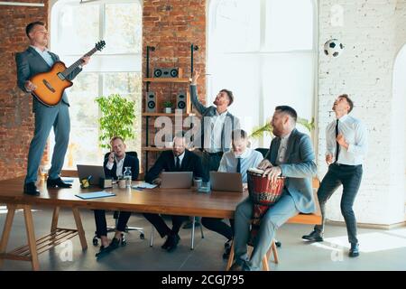 Cantare, dare concerti di musica, ballare. I colleghi sono felici e spensierati e si divertono in ufficio mentre i colleghi lavorano sodo e altamente concentrati. Concetto di divertimento, riposo, occupazione professionale. Foto Stock