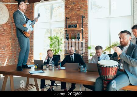 Cantare, dare concerti di musica, ballare. I colleghi sono felici e spensierati e si divertono in ufficio mentre i colleghi lavorano sodo e altamente concentrati. Concetto di divertimento, riposo, occupazione professionale. Foto Stock