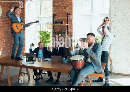 Cantare, dare concerti di musica, ballare. I colleghi sono felici e spensierati e si divertono in ufficio mentre i colleghi lavorano sodo e altamente concentrati. Concetto di divertimento, riposo, occupazione professionale. Foto Stock