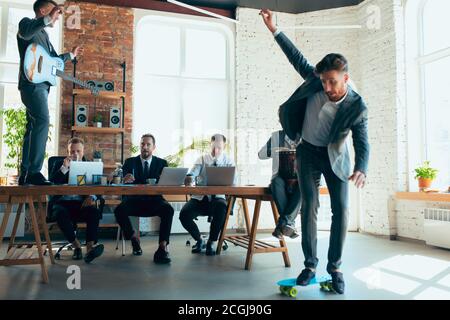 Cantare, dare concerti di musica, ballare. I colleghi sono felici e spensierati e si divertono in ufficio mentre i colleghi lavorano sodo e altamente concentrati. Concetto di divertimento, riposo, occupazione professionale. Foto Stock