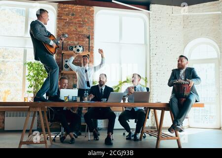 Cantare, dare concerti di musica, ballare. I colleghi sono felici e spensierati e si divertono in ufficio mentre i colleghi lavorano sodo e altamente concentrati. Concetto di divertimento, riposo, occupazione professionale. Foto Stock