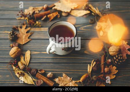 Tazza di metallo rustica con tè e corona d'autunno fatta di foglie, bacche, ghiande e coni di pino su sfondo di legno scuro. Ciao autunno! Accogliente immagine autunnale Foto Stock