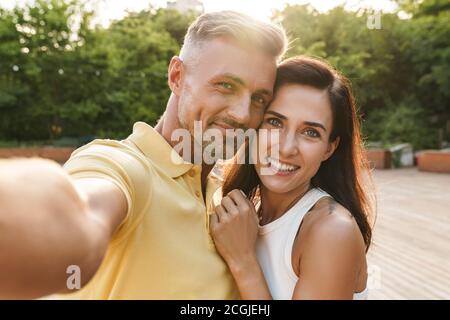 Ritratto di felice di mezza età giovane uomo e donna prendendo selfie foto e abbracciando mentre passeggiate in estate park Foto Stock