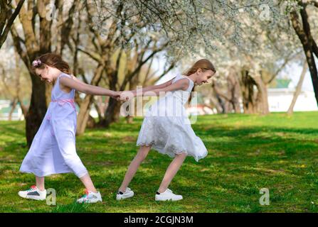 Belle ragazze con occhi blu in abiti bianchi nel giardino con alberi di mela che si profilano divertendosi e. godendo l'odore di gar di primavera fiorito Foto Stock