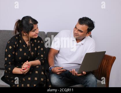 Giovane coppia indiana che usa il computer portatile seduto su un divano. Foto Stock