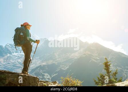 Giovane escursionista zaino in spalla femmina utilizzando pali da trekking godendo di vista montagna durante l'alta altitudine acclimatazione passeggiata. Percorso di trekking Everest base Camp, Foto Stock