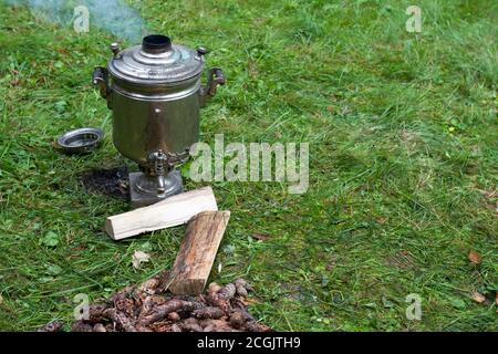 Riscaldamento del samovar con coni per la preparazione del tè. Il samovar si trova sull'erba. Fumo dal tubo Foto Stock