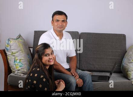 Giovane coppia indiana che usa il computer portatile seduto su un divano. Foto Stock