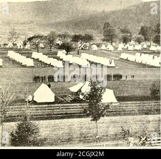 . La storia fotografica della Guerra civile : in dieci volumi . REVISIONE DI RENEWS CIAO. CAMBIANDO LA GUARDIA ALLA PRIGIONE DI ELMIRA, 1864 questa fotografia dei quartieri delle guardie che hanno tenuto sotto controllo le migliaia di prigionieri confederati confinati a Elmira mostra che le condizioni erano molto migliori fuori dal campo che in. Le lunghe ombre delle linee regolari di tende indicano chiaramente che è stato preso nel tardo pomeriggio. Il fogliame sugli alberi fissa la stagione come estate. Gli uomini sono apparentemente impegnati in cambio di guardia. Il Dott. E. F. Sanger, il chirurgo attaccato a Elmira, ha avuto grande difficoltà nell'ottenere h Foto Stock