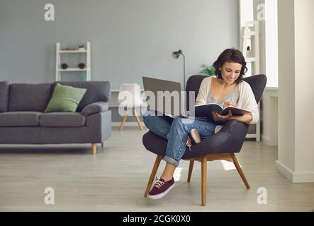 Donna sorridente seduto a casa con un computer portatile e prendere appunti durante la lezione online Foto Stock